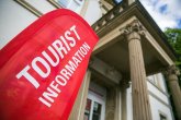 Touristinformation Im Hintergund das Gebäude der Touristinformation. Im Vordergrund eine rote Fahne mit der Aufschrift Touristinformation.