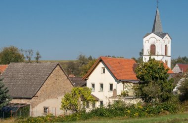 Kirche, einige alte Gebäude, blauer Himmel, grüne Wiese, einige Bäume und Sträucher