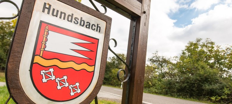 Foto eines Holzschildes mit Wappen und Name der Ortsgemeinde Hundsbach.