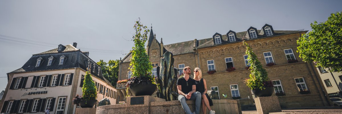 Marktplatz Bad Sobernheim Marktplatz mit Brunnen auf dessen Rand ein Mann und eine Frau in der Sonne sitzten