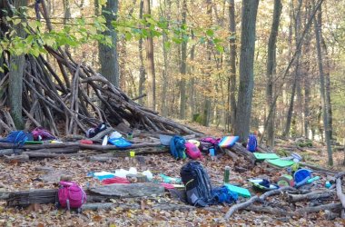 Foto einiger Kinderrucksäcke, Kleidungsstücke und Getränkeflaschen im Wald.
