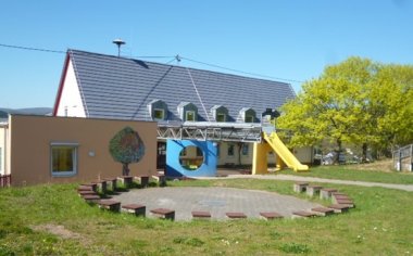Foto der Rückansicht des Kindergartens der Ortsgemeinde Monzingen mit Blick auf Sitzgelegenheiten, eine Rutsche und Spielbereiche