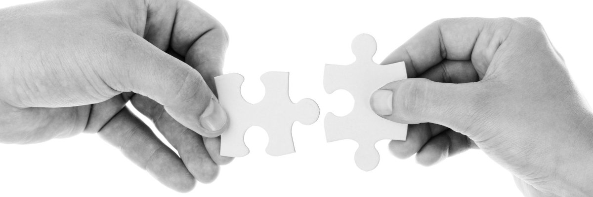 Symbolbild Schwarz-Weiß-Fotografie zweier gegenüberliegender Hände, die jeweils ein zu ihrem Gegenüber passendes Puzzleteil halten.